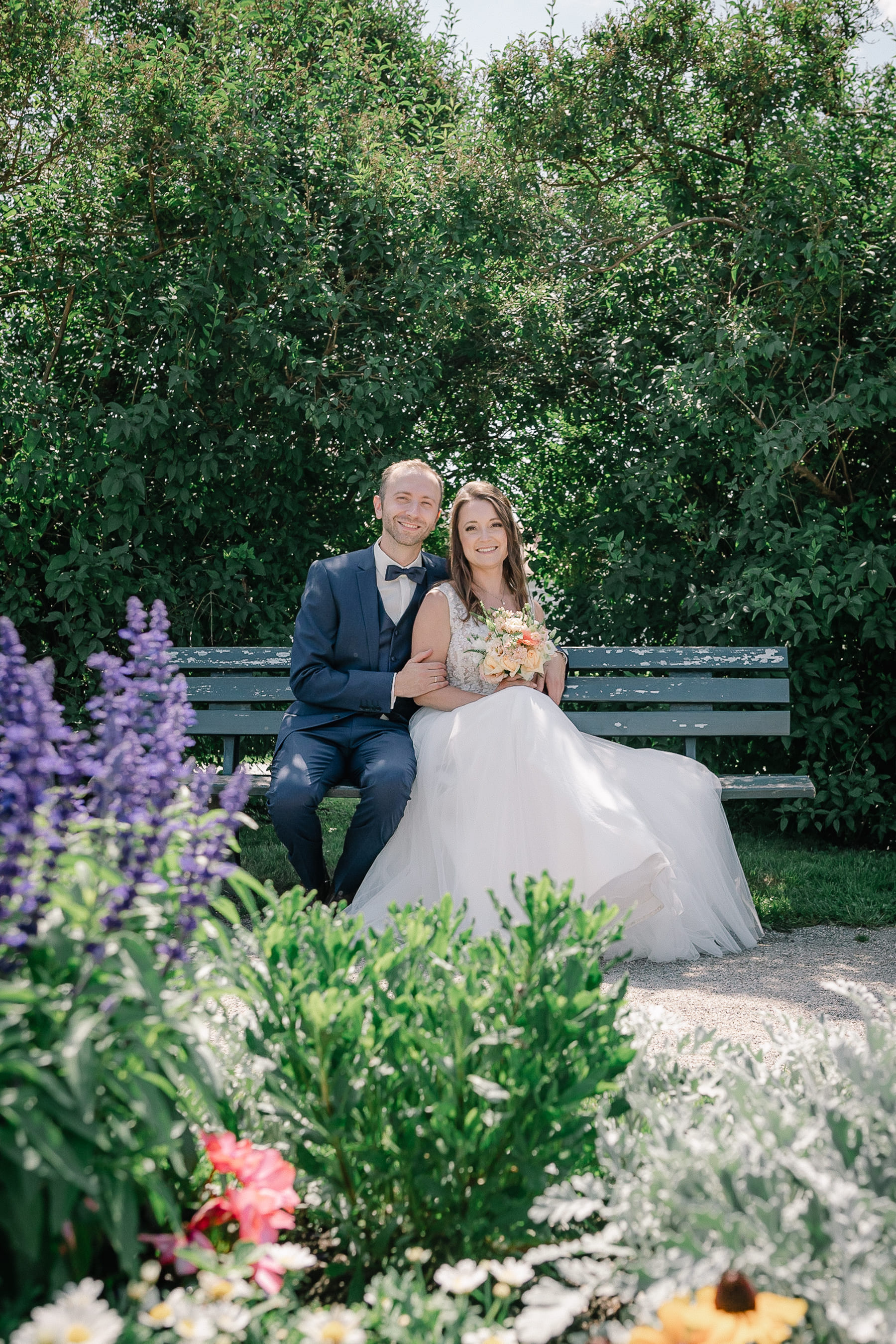 Hochzeitsfoto auf einer Parkbank rundherum Blumen